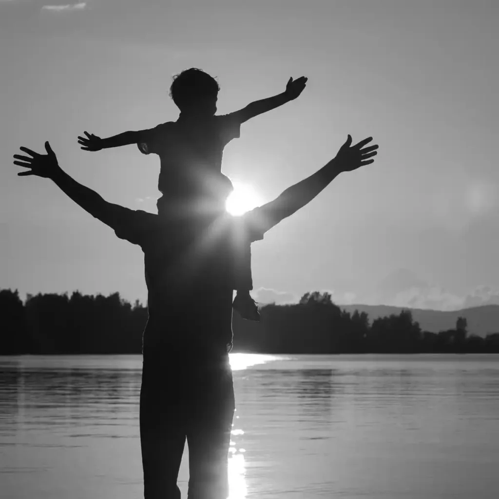 Father carrying young son on his shoulders overlooking a lake at sunset