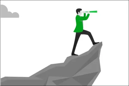 A man stands on a cliff looking ahead with a telescope.